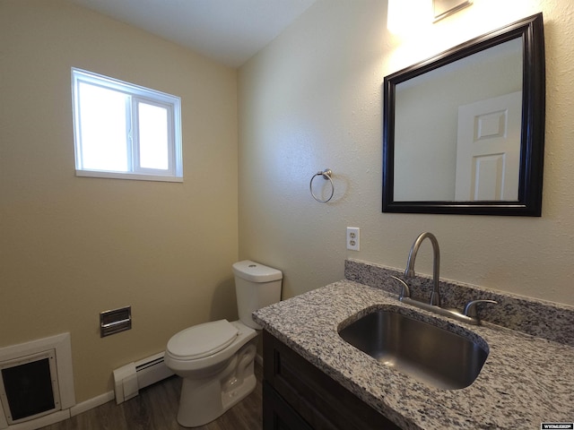 half bathroom featuring a baseboard heating unit, vanity, toilet, and wood finished floors