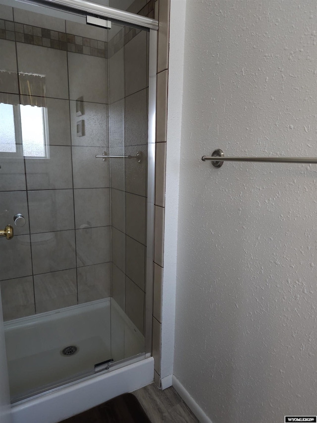 full bath with a shower stall, wood finished floors, baseboards, and a textured wall