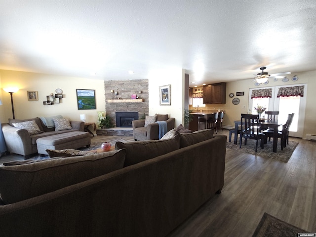 living room with a fireplace, a textured ceiling, dark wood-type flooring, and a ceiling fan