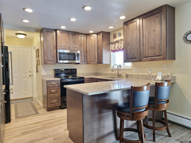 kitchen featuring a peninsula, electric range, a sink, a kitchen bar, and stainless steel microwave