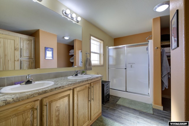 full bath featuring double vanity, a stall shower, wood finished floors, and a sink