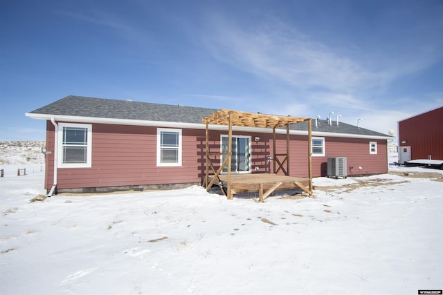 snow covered rear of property featuring central air condition unit and a shingled roof