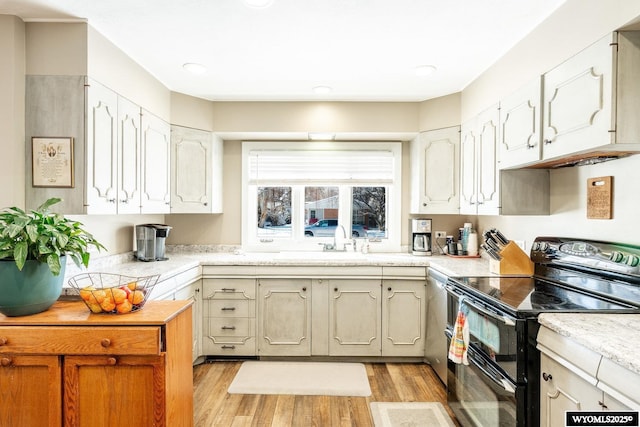 kitchen featuring double oven range, a sink, light countertops, light wood-style floors, and white cabinetry