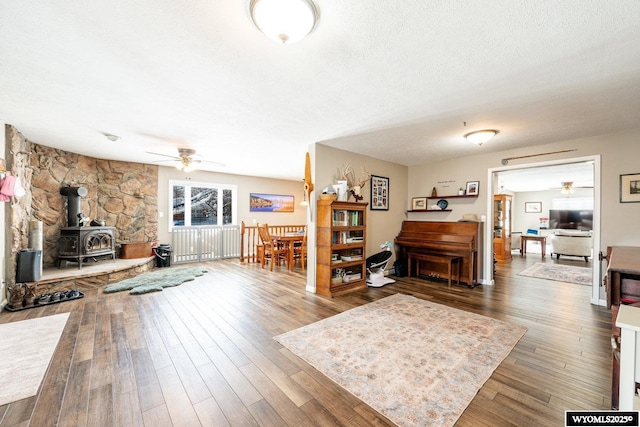 living area featuring a textured ceiling, a wood stove, a ceiling fan, and wood finished floors