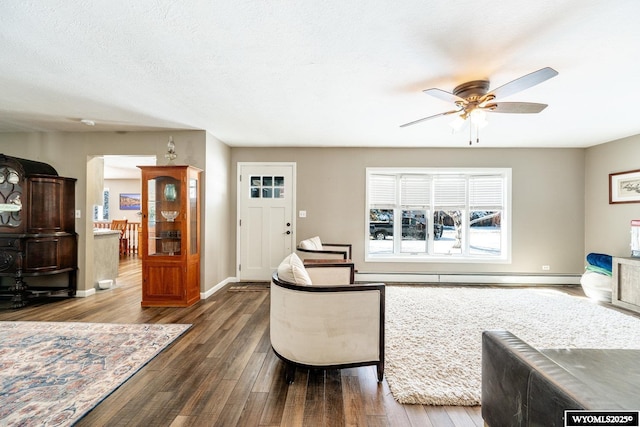 living room featuring a baseboard heating unit, ceiling fan, baseboards, wood finished floors, and a textured ceiling