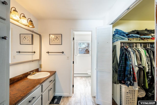 bathroom featuring a spacious closet, toilet, wood finished floors, vanity, and a baseboard radiator