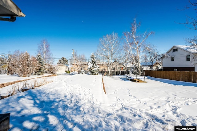 snowy yard featuring a trampoline, fence, and a residential view