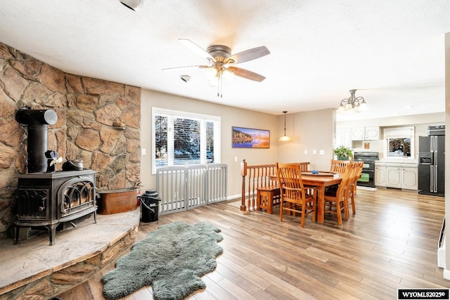 dining room with light wood-style flooring, a ceiling fan, a wood stove, and a textured ceiling