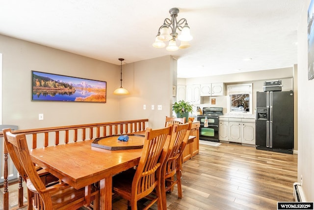 dining space featuring light wood finished floors, a chandelier, and a baseboard heating unit