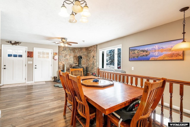 dining space with ceiling fan, baseboards, a wood stove, wood finished floors, and a textured ceiling