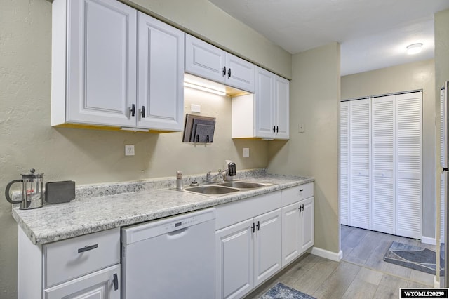 kitchen featuring light wood finished floors, a sink, white cabinets, light countertops, and dishwasher