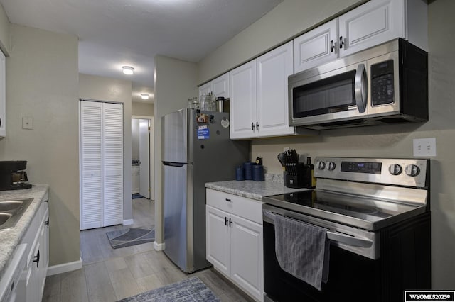 kitchen with light countertops, light wood-style flooring, stainless steel appliances, white cabinetry, and a sink