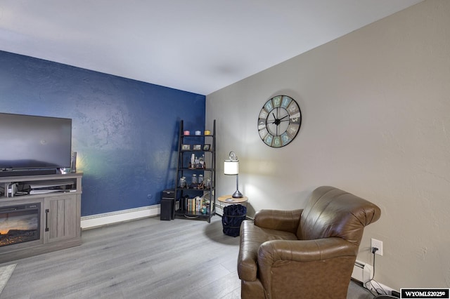 sitting room with a baseboard heating unit, wood finished floors, and baseboards