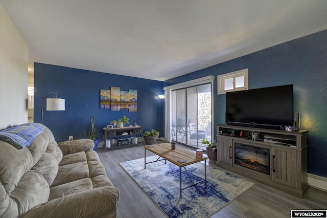 living area with a glass covered fireplace, baseboards, and wood finished floors