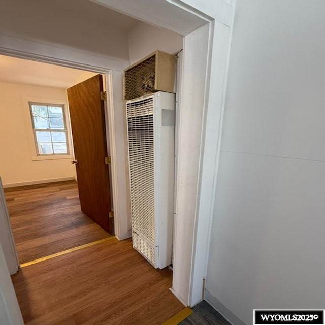 hallway with baseboards, wood finished floors, and a heating unit