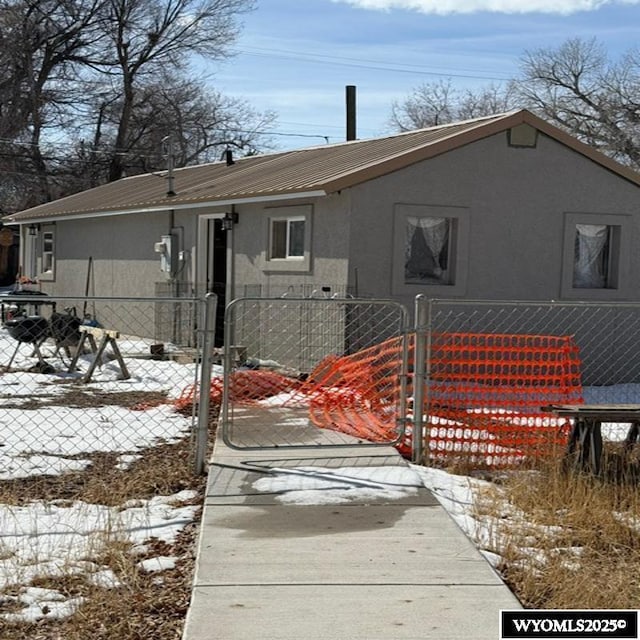 snow covered rear of property featuring a fenced front yard, stucco siding, and a gate