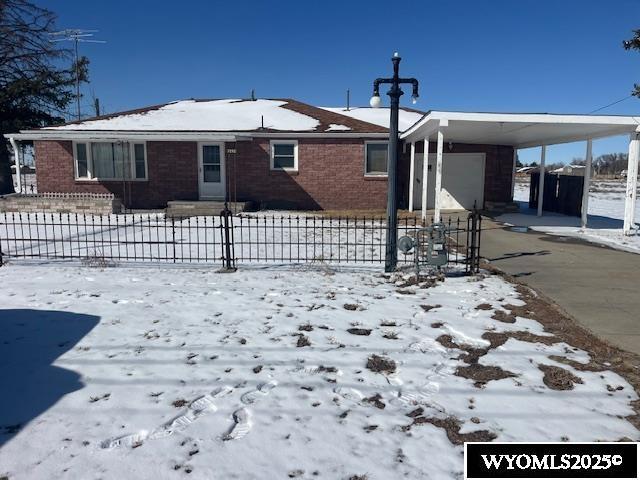 snow covered property featuring a fenced front yard, driveway, a carport, and brick siding