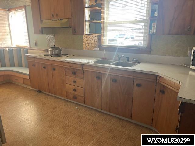 kitchen with light countertops, plenty of natural light, under cabinet range hood, and a sink