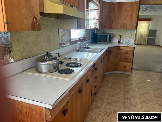 kitchen with stainless steel microwave, under cabinet range hood, light countertops, brown cabinets, and a sink