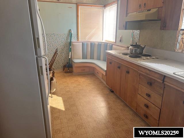 kitchen with under cabinet range hood, white appliances, light floors, and light countertops