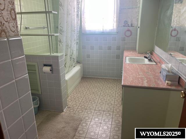 full bath featuring shower / bath combo with shower curtain, tile walls, and vanity