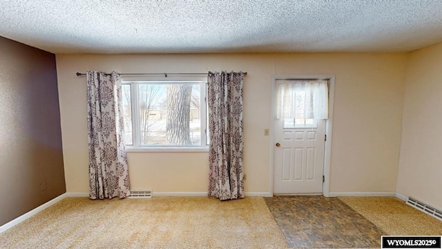 foyer entrance with visible vents, baseboards, a textured ceiling, and carpet flooring