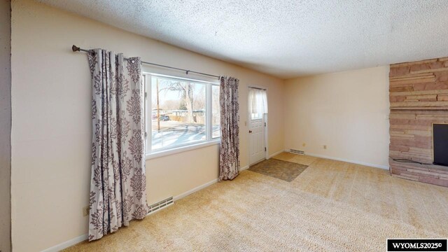 carpeted entryway featuring visible vents, baseboards, a textured ceiling, and a fireplace