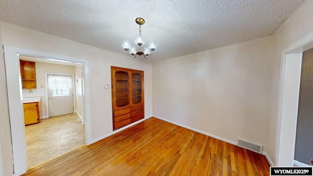 unfurnished dining area featuring a notable chandelier, visible vents, light wood finished floors, and a textured ceiling