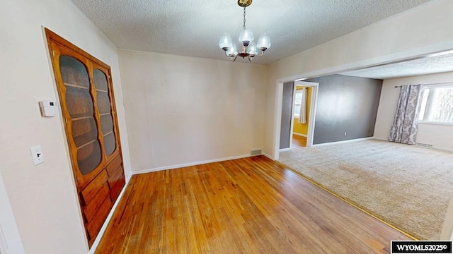 carpeted spare room featuring visible vents, baseboards, wood finished floors, a notable chandelier, and a textured ceiling