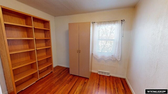 unfurnished bedroom featuring visible vents, baseboards, a closet, and wood finished floors