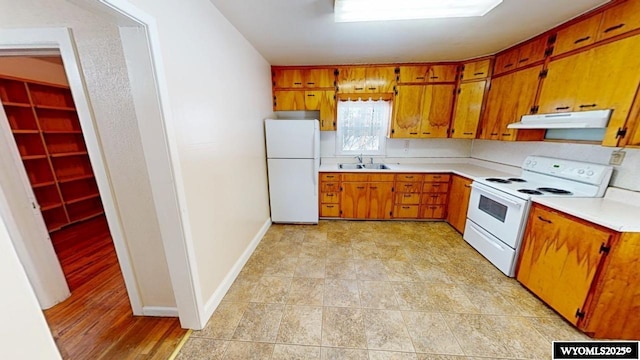 kitchen with white appliances, a sink, light countertops, under cabinet range hood, and brown cabinets