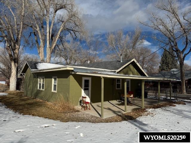 snow covered rear of property featuring a patio and concrete block siding