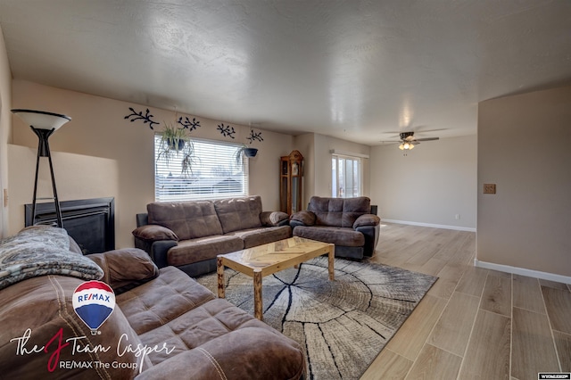 living area with ceiling fan, a fireplace, baseboards, and wood finish floors