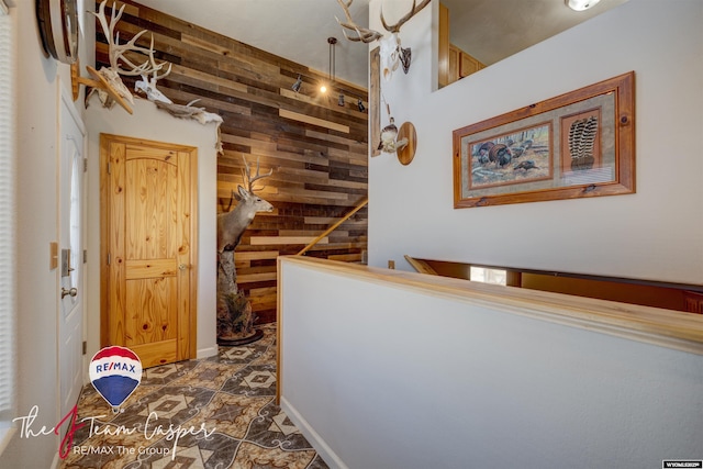 hallway featuring wooden walls, an upstairs landing, and stone finish flooring