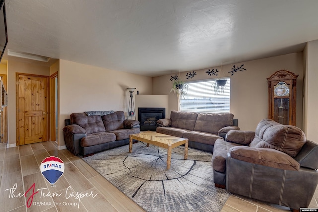 living area featuring a glass covered fireplace, baseboards, and wood tiled floor