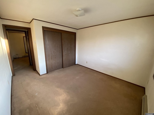 unfurnished bedroom with a baseboard heating unit, crown molding, a closet, and light carpet