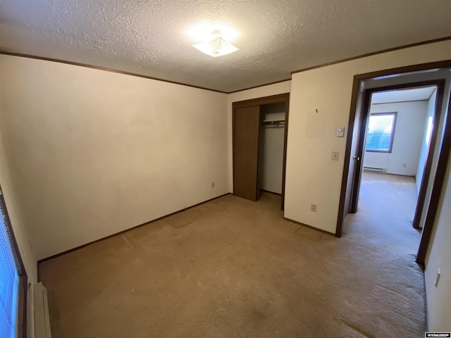 unfurnished bedroom with a baseboard radiator, a closet, a textured ceiling, crown molding, and light carpet