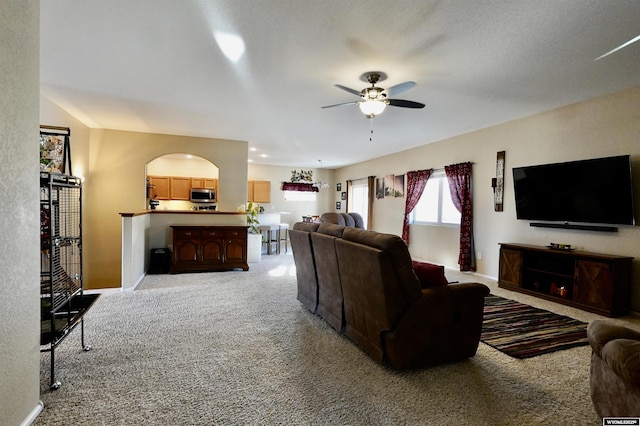 living area featuring baseboards, light colored carpet, ceiling fan, and arched walkways