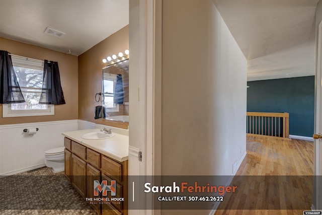 bathroom with visible vents, toilet, wood finished floors, wainscoting, and vanity