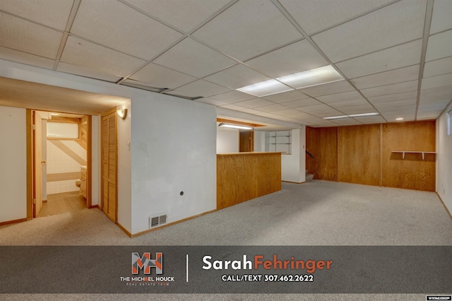 finished below grade area featuring visible vents, wood walls, a paneled ceiling, and carpet