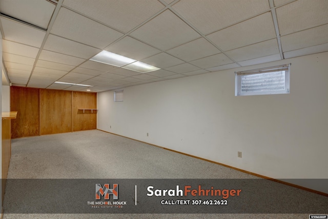 below grade area with a drop ceiling, wood walls, baseboards, and carpet