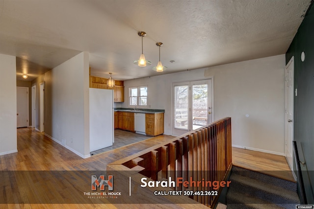 kitchen featuring dark countertops, light wood-style floors, white appliances, a textured ceiling, and a sink