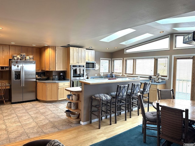 kitchen with a breakfast bar area, recessed lighting, stainless steel appliances, light countertops, and lofted ceiling with skylight