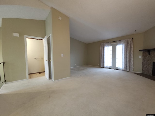 unfurnished living room with baseboards, vaulted ceiling, light carpet, french doors, and a fireplace