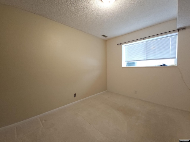 spare room featuring visible vents, light carpet, a textured ceiling, and baseboards