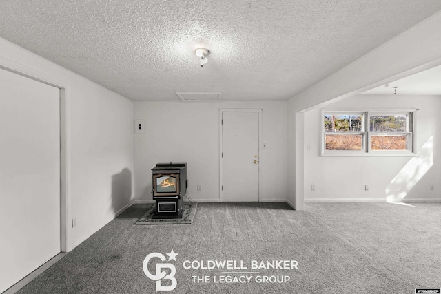 interior space featuring carpet flooring, baseboards, a textured ceiling, and a wood stove