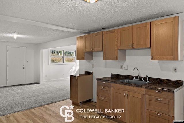 kitchen with light wood-type flooring, brown cabinets, a sink, a textured ceiling, and dark stone counters