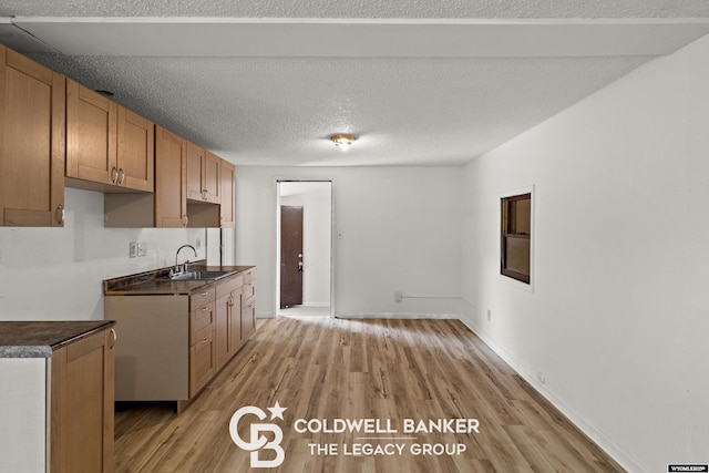 kitchen with light wood-type flooring, a sink, dark countertops, a textured ceiling, and baseboards