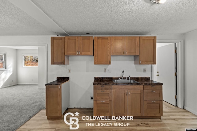 kitchen featuring a sink, light wood-type flooring, a textured ceiling, and brown cabinetry