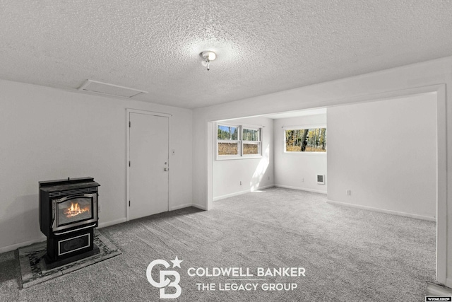 spare room with baseboards, attic access, a wood stove, a textured ceiling, and carpet flooring